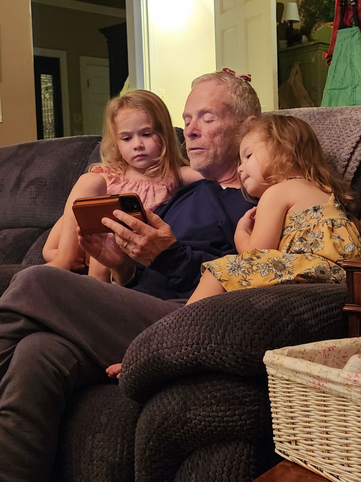 Bob Massie seated on a couch with two young girls nestled against him, looking at a phone together.