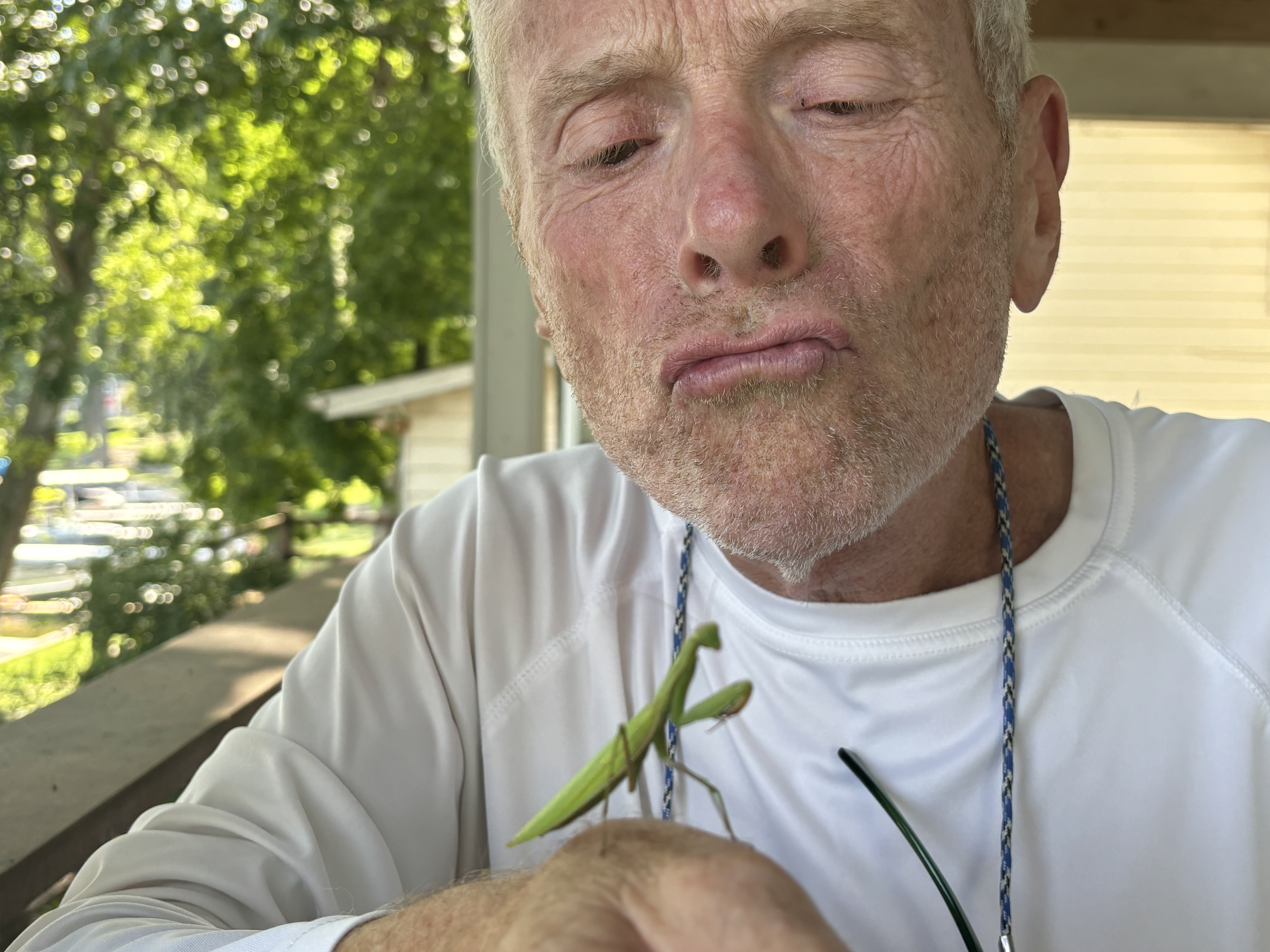 Close-up of Bob Massie regarding a praying mantis perched on his hand, outdoors.