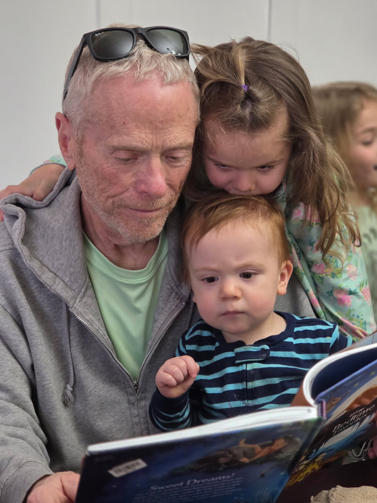 Bob Massie reading a picture book with three grandchildren gathered around him.